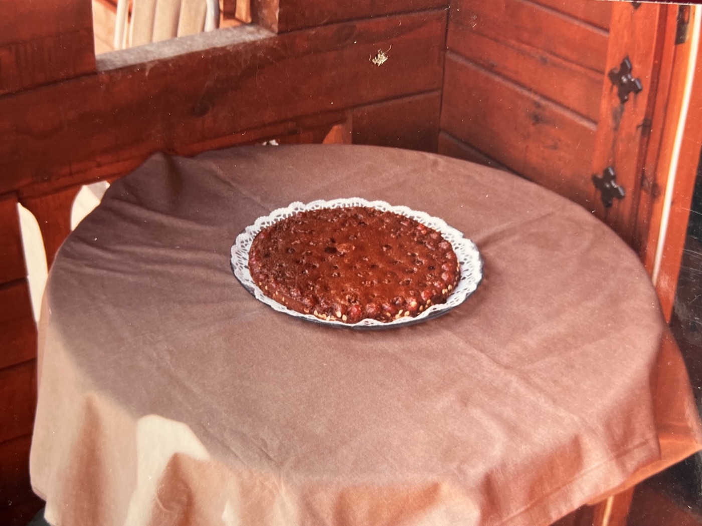 Un pie sobre una mesa redonda con mantel rosado, junto a una ventana de madera