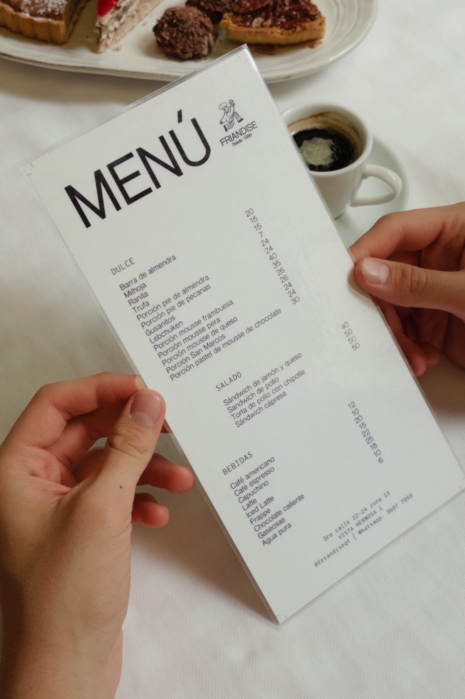 Manos sosteniendo el menú de Friandise sobre una mesa con café y postres